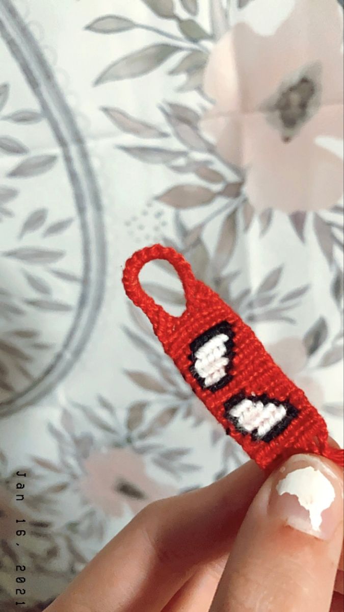 someone is holding up a small crocheted red object with white hearts on it