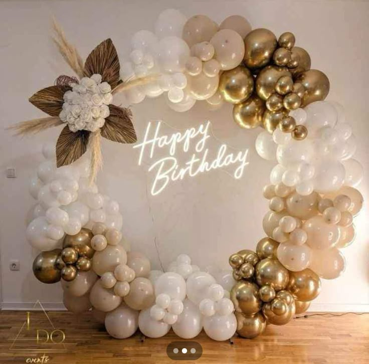 a happy birthday balloon arch with flowers and balloons in the shape of a wreath on a wooden floor