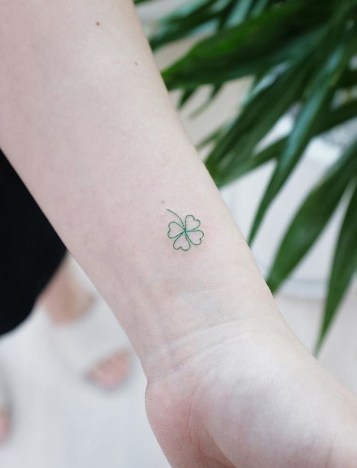 a small four leaf clover tattoo on the left inner arm and wrist, with green leaves in the background