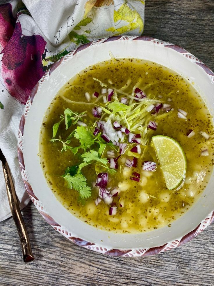 a white bowl filled with green soup and garnished with cilantro, red onion, and lime