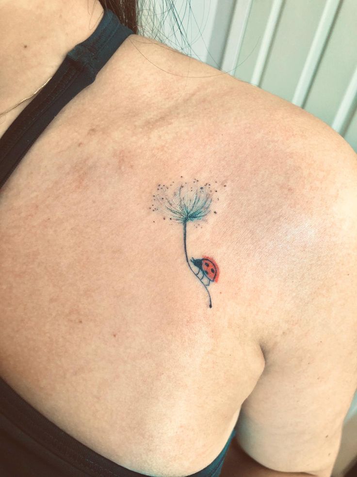 the back of a woman's shoulder with a dandelion tattoo on it