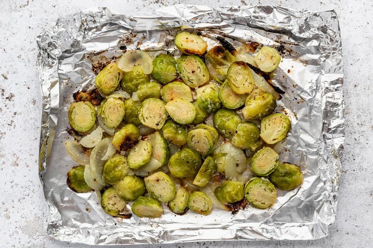 roasted brussel sprouts on aluminum foil in a square baking dish, ready to be cooked