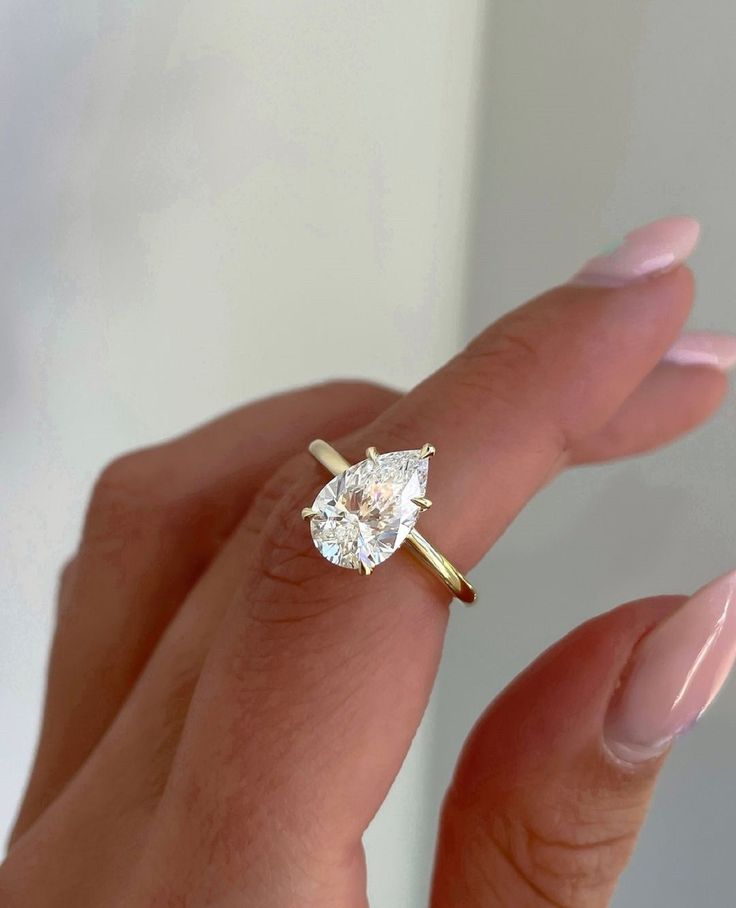 a woman's hand holding a ring with a pear shaped diamond on it,