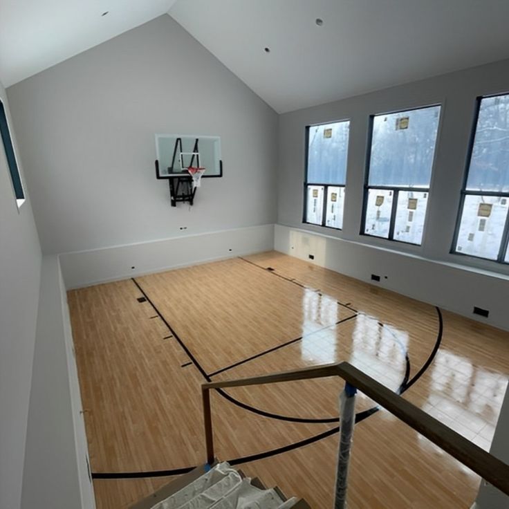 an empty basketball court in the middle of a room with three windows and a basketball hoop hanging on the wall