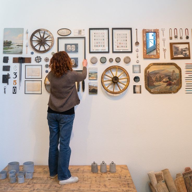 a woman standing in front of a wall full of clocks and other items on display