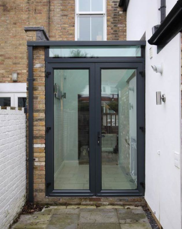 an outside view of a house with glass doors and brick walkway leading to the back door