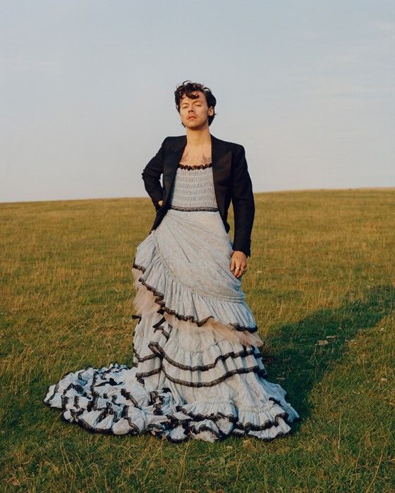 a woman in a dress and jacket standing on the grass