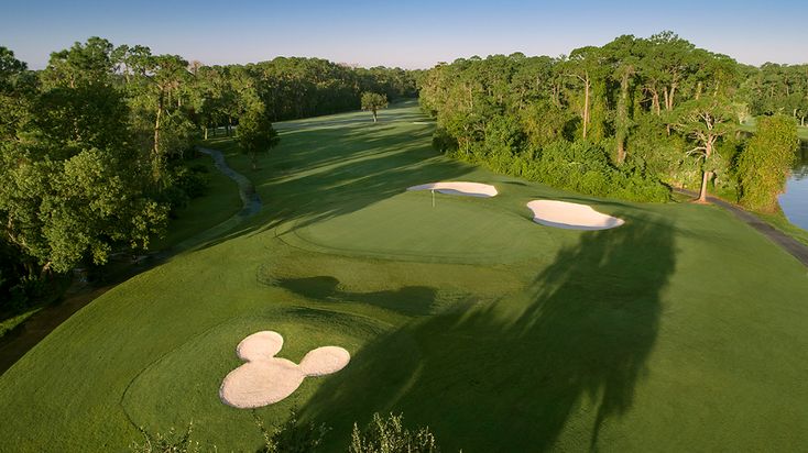 an aerial view of a golf course with water and trees in the background at sunset