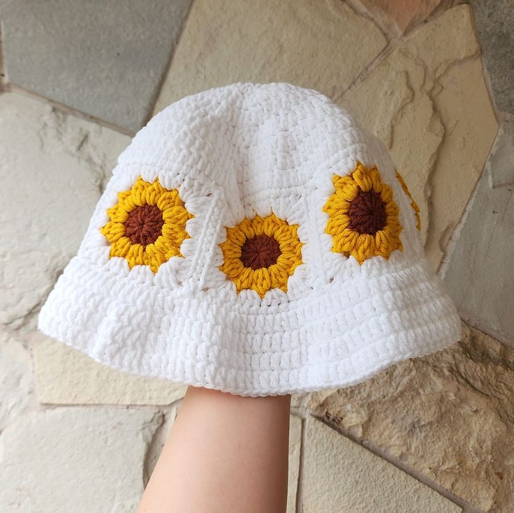 a white hat with sunflowers on the front and side, sitting on top of a stone floor