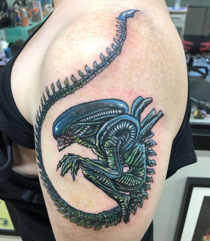 an alien tattoo on the back of a man's arm, with green and black ink