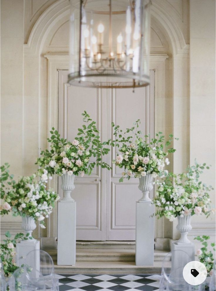 flowers are in vases on the checkered floor next to an ornate door and chandelier