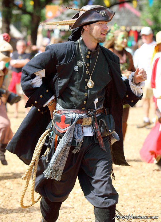 a man dressed in pirate garb walking through the park with other people around him