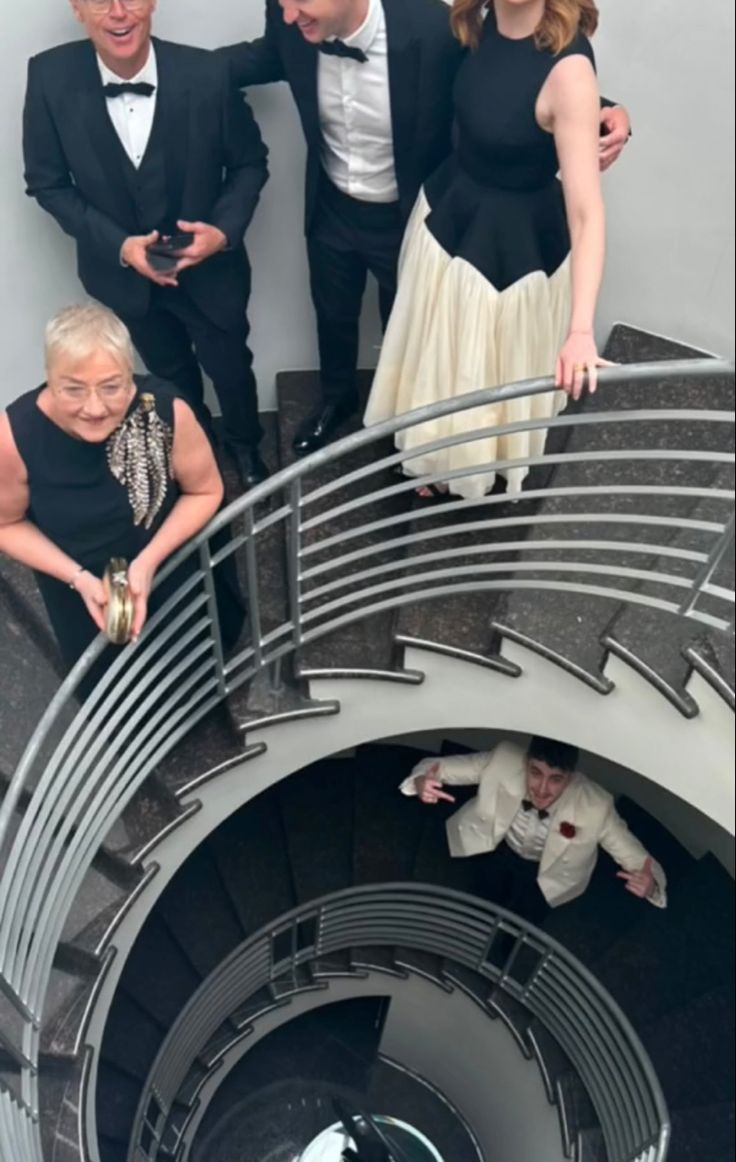 three men and two women are standing on a spiral staircase