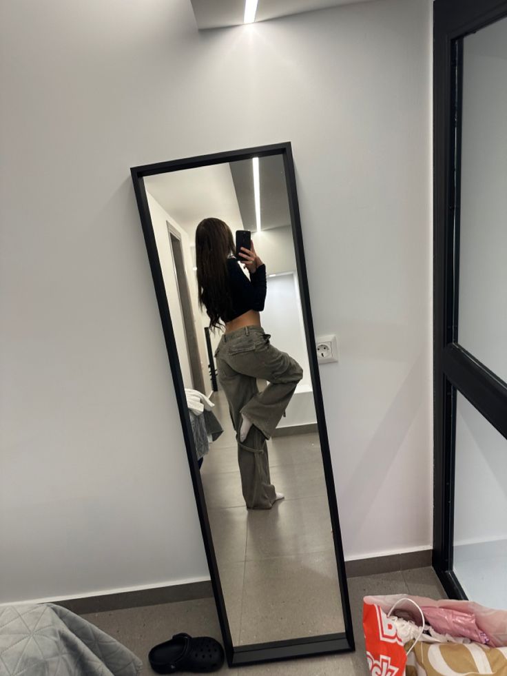 a woman taking a selfie in front of a mirror with her pants and shoes on