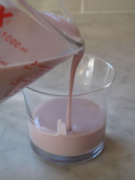 a pitcher pouring milk into a glass filled with pink liquid