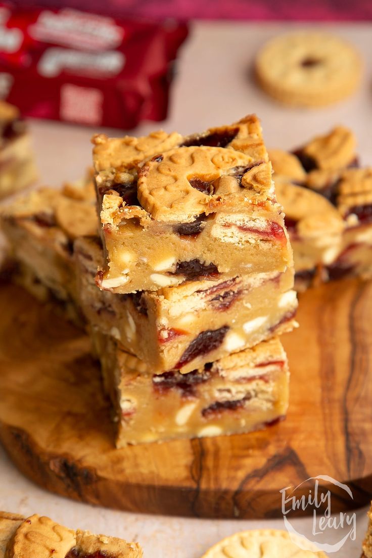 several pieces of dessert sitting on top of a wooden cutting board next to some cookies