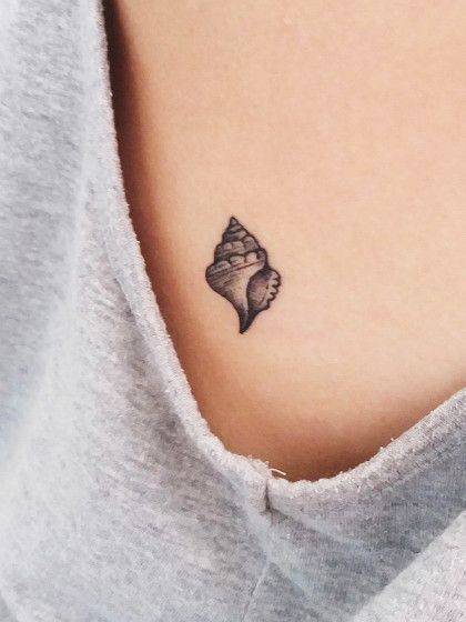 a woman's chest with a small tattoo of a seashell on her left side