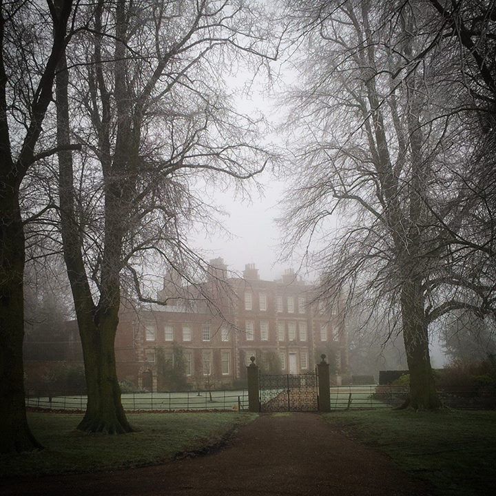 an old house in the middle of a park with lots of trees on both sides