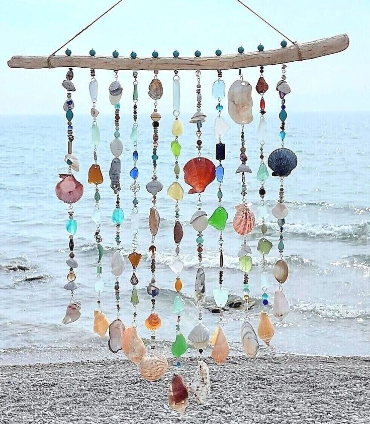 a wind chime hanging on the beach with sea glass beads and seashells