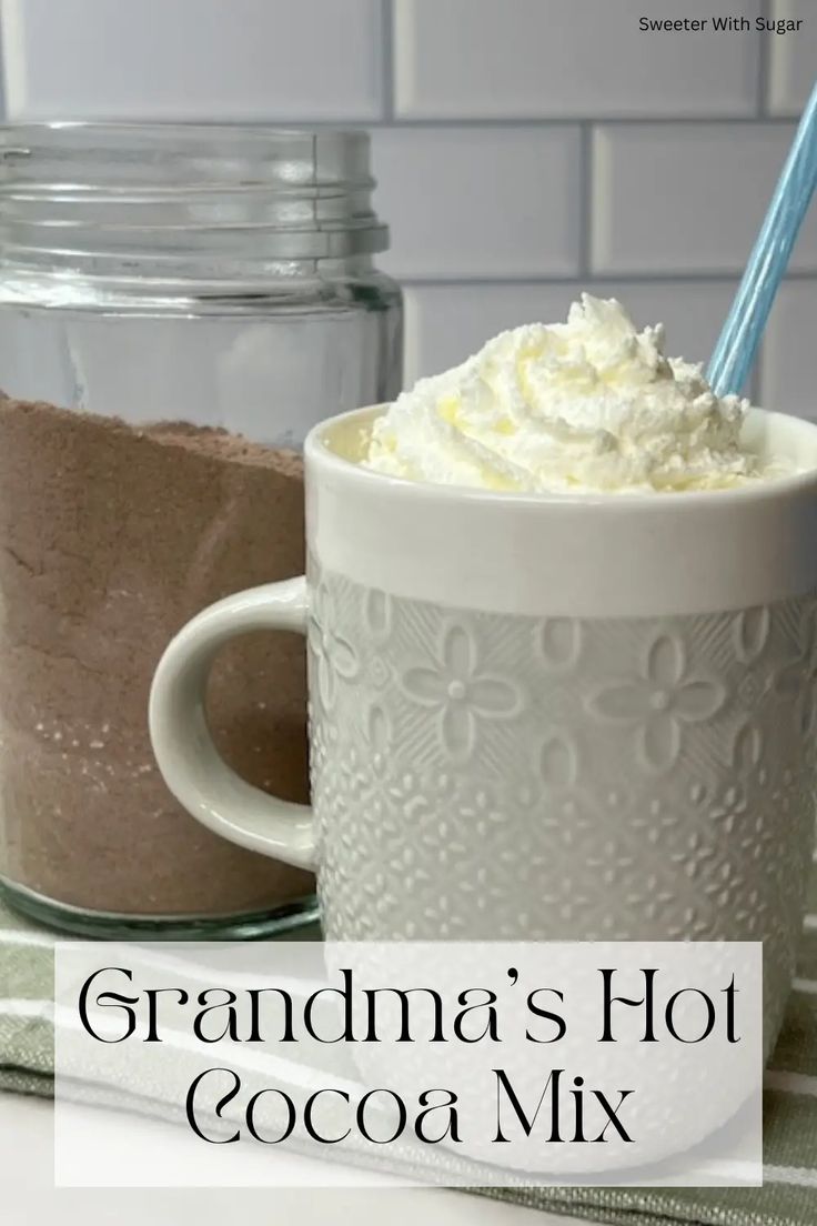 a mug with whipped cream in it sitting on a counter next to a jar of cocoa