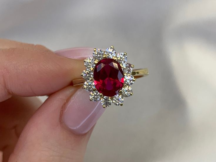 a woman's hand holding a ring with a red stone surrounded by white diamonds