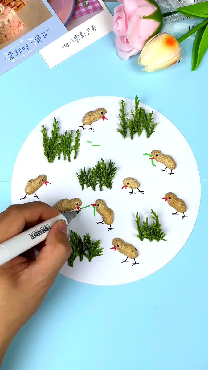 someone is making a paper plate with birds and pine branches on it, surrounded by pink tulips