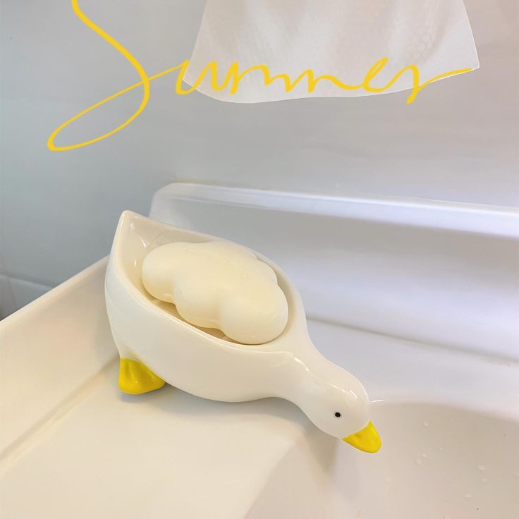 a duck shaped soap dish sitting on the edge of a bathtub next to a towel rack