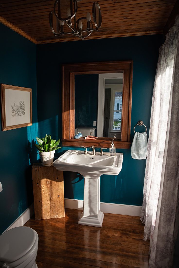 a bathroom with blue walls and wood flooring has a white pedestal sink in the corner