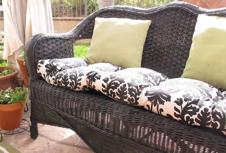 a wicker couch with pillows on it in front of some plants and potted plants