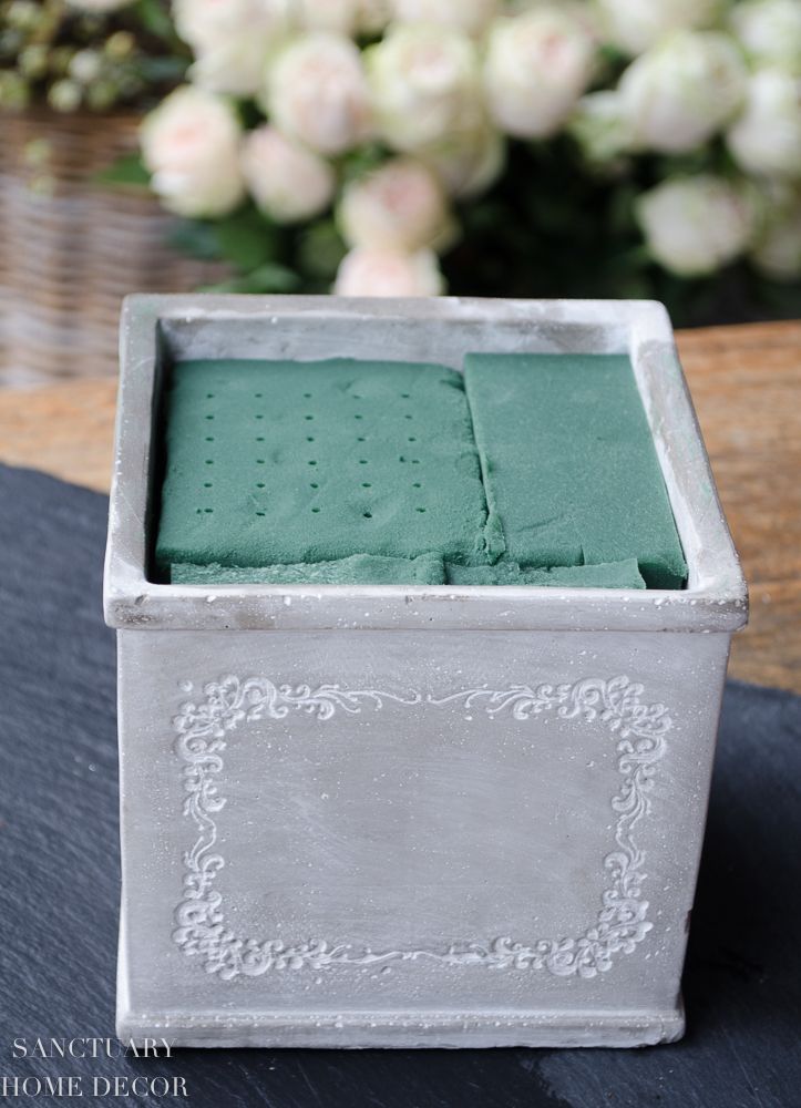 a small white box with green tissue in it sitting on a table next to flowers