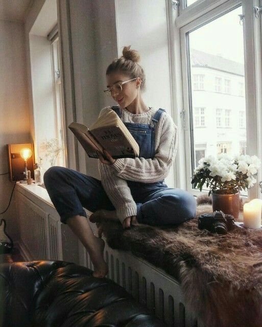 a woman sitting on a window sill reading a book