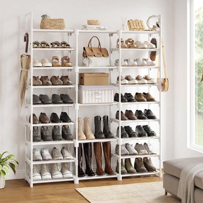 a white shoe rack filled with shoes next to a couch in a living room under a window