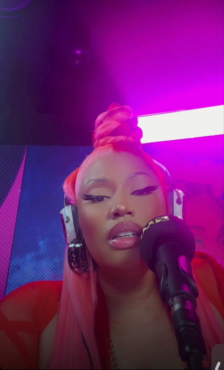 a woman with pink hair and headphones on her ear is singing into a microphone