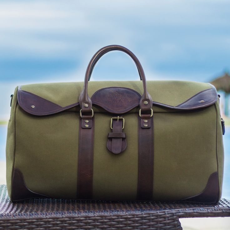 DESCRIPTION: The Wingfield Canvas & Leather Duffel Bag is crafted from premium canvas and vegetable-tanned leather with old brass color hardware and zipper. With ample space for traveling or any occasion, this duffle bag is both stylish and functional. Enjoy the luxury and versatility of this expertly crafted accessory.  FEATURES:  Premium canvas.  Vegetable tanned leather.  Premium Zipper.  Inner cotton lining.  Leather/textile adjustable strap.   SIZE:   22.5 " X 11 " X 9.5"  38.5 Lts Green Duck Canvas Travel Bag, Khaki Canvas Duffle Bag For Travel, Travel Duffle Bag In Khaki Canvas, Green Weekender Bag With Leather Handles For Travel, Green Canvas Duffle Bag For Travel, Green Leather Travel Weekender Bag, Khaki Leather Travel Satchel, Leather Khaki Satchel For Travel, Green Leather Weekender Bag For Travel