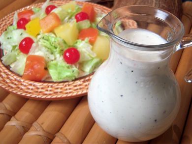 a bowl of salad next to a pitcher of milk on a table with a plate of fruit