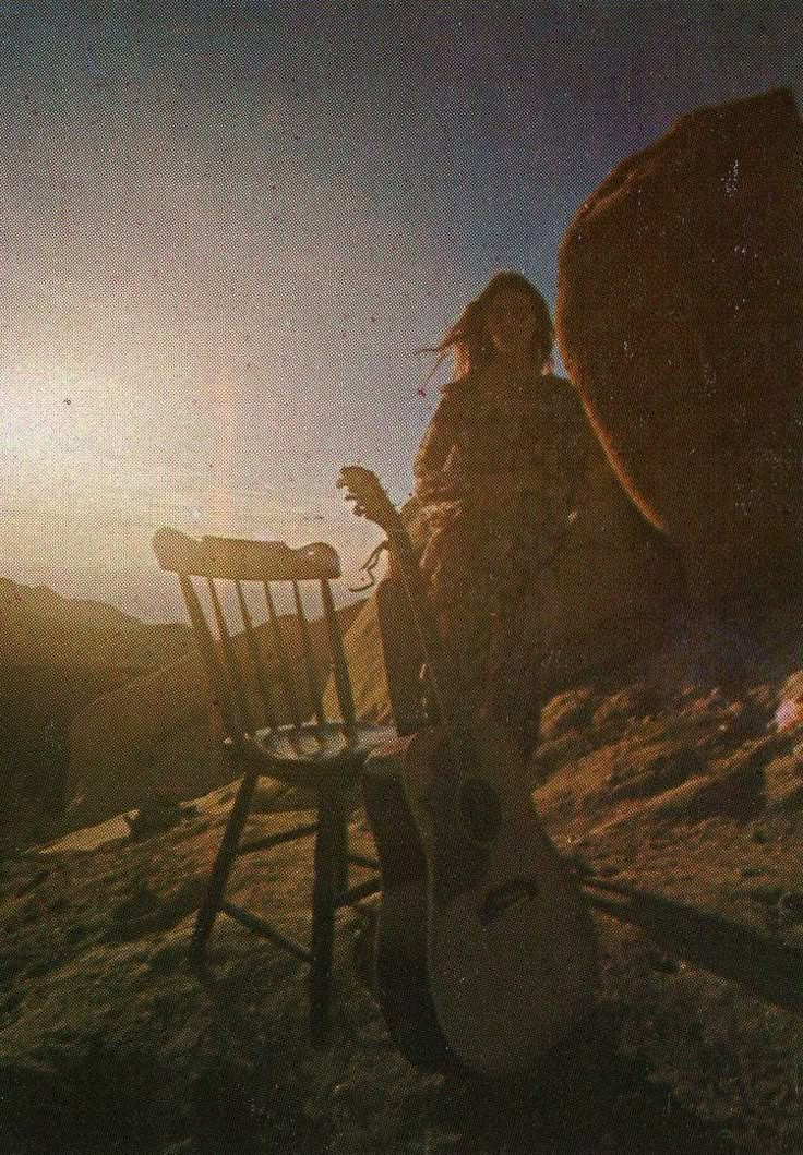 a woman sitting on top of a wooden chair next to a guitar