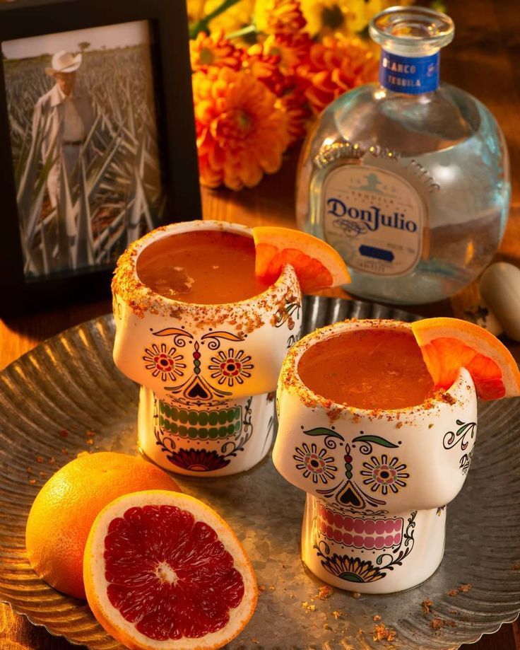 two glasses filled with blood oranges on top of a metal tray next to an empty bottle