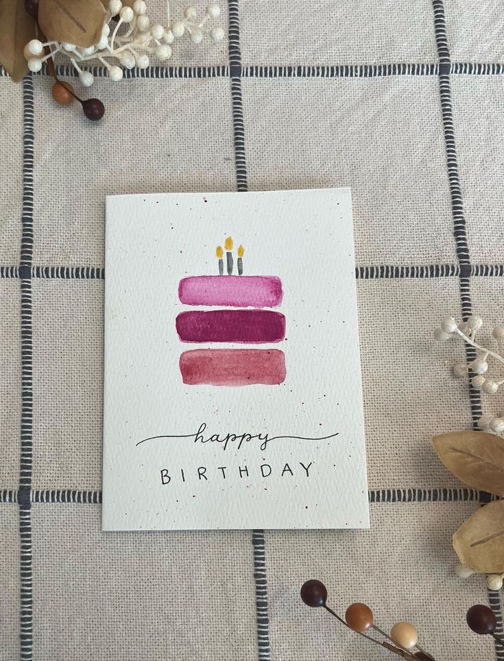 a birthday card with a cake on it sitting on a table next to some flowers