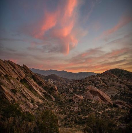 the sun is setting in the mountains with pink and blue clouds above it, as seen from an overlook point