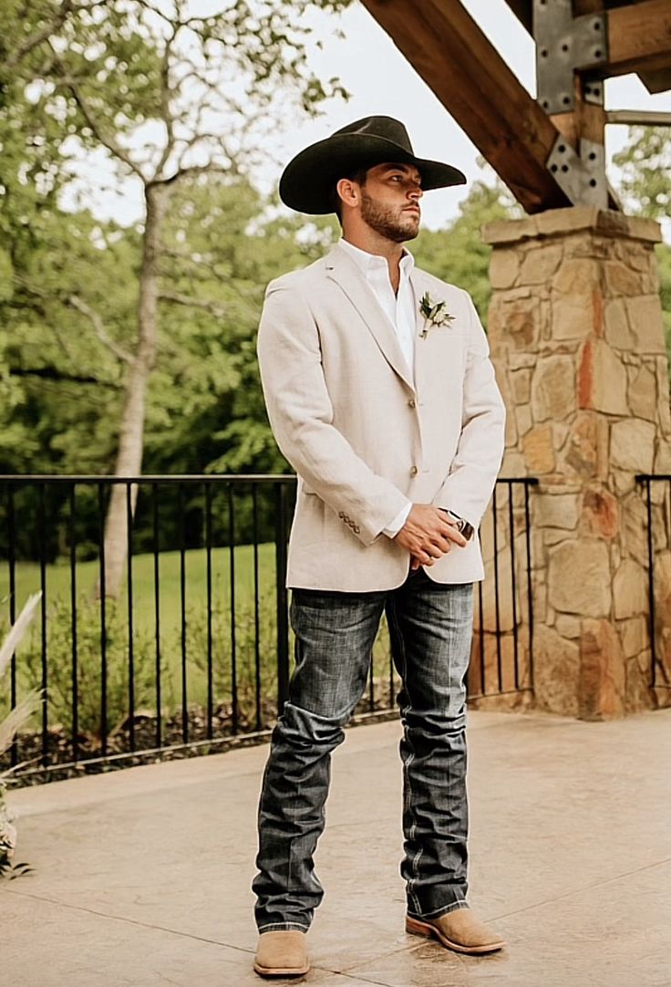 a man wearing a cowboy hat standing in front of a stone pillar and black iron fence