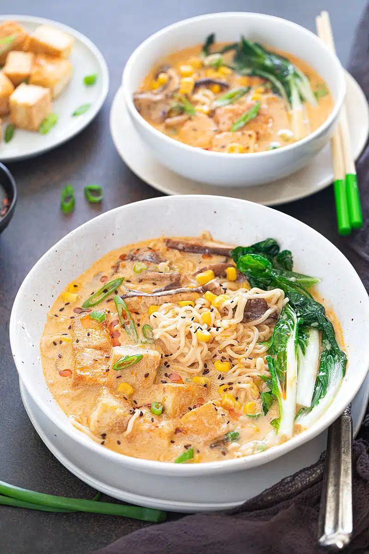 two white bowls filled with soup next to green onions and broccoli on a table