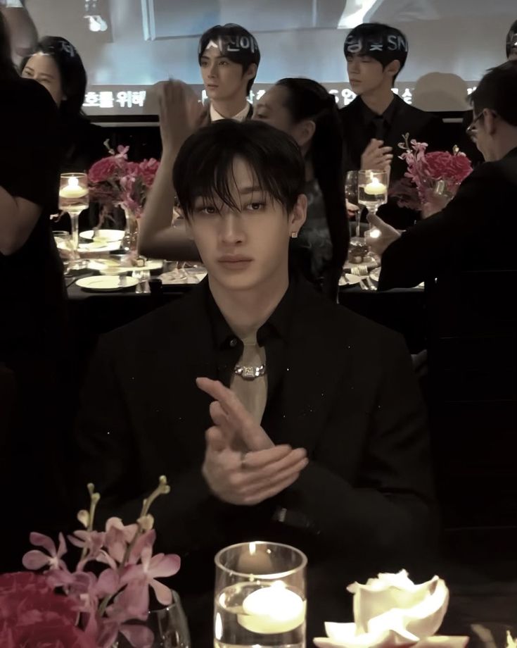 a man in a suit sitting at a table with flowers and wine glasses on it