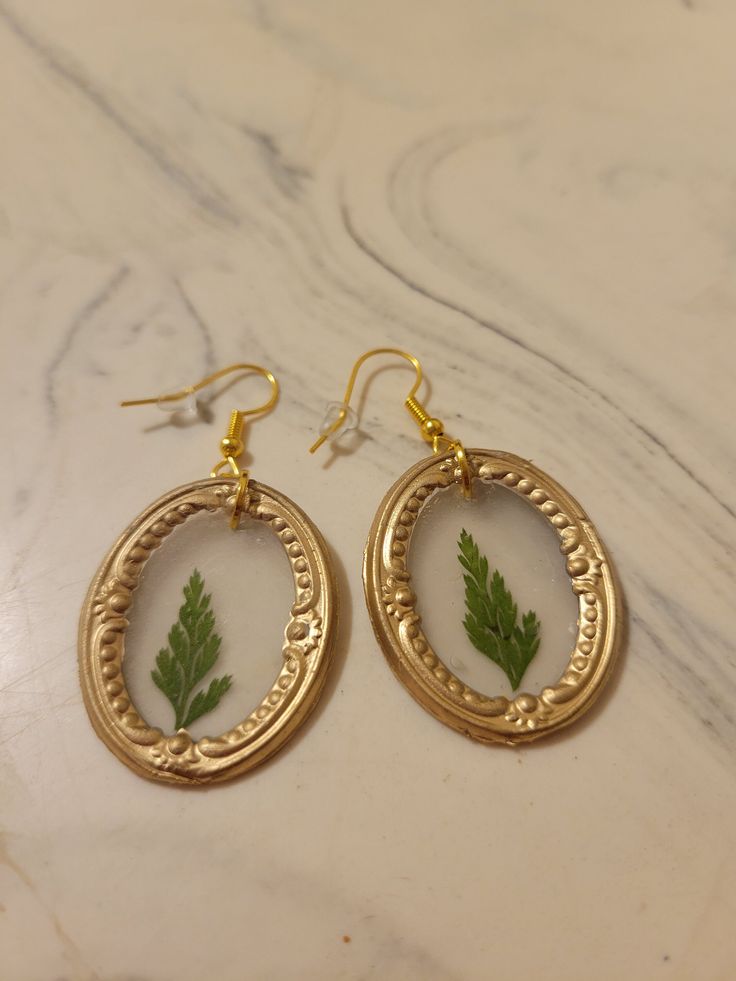 "These framed pressed flower earrings are handmade and use crystal clear hot glue to allow the flower to be seen inside the frame. The earring hooks are hypoallergenic, gold-plated stainless steel and come with a rubber back. The framed pressed flowers measure 1.25\"x1\" for the oval frame and 1\"x0.75\" for the rectangular frame. The flower color and frame shape can be customized." Gold Resin Earrings With Birth Flower Detail, Gold Resin Earrings With Birth Flower, Nature-inspired Gold Earrings With Pressed Flowers, Nature-inspired Gold Flower Earrings With Pressed Flowers, Gold Botanical Earrings With Pressed Flowers, Botanical Gold Earrings With Pressed Flowers, Botanical Style Gold Resin Jewelry, Handmade Gold Botanical Earrings, Botanical Gold Earrings With Birth Flower