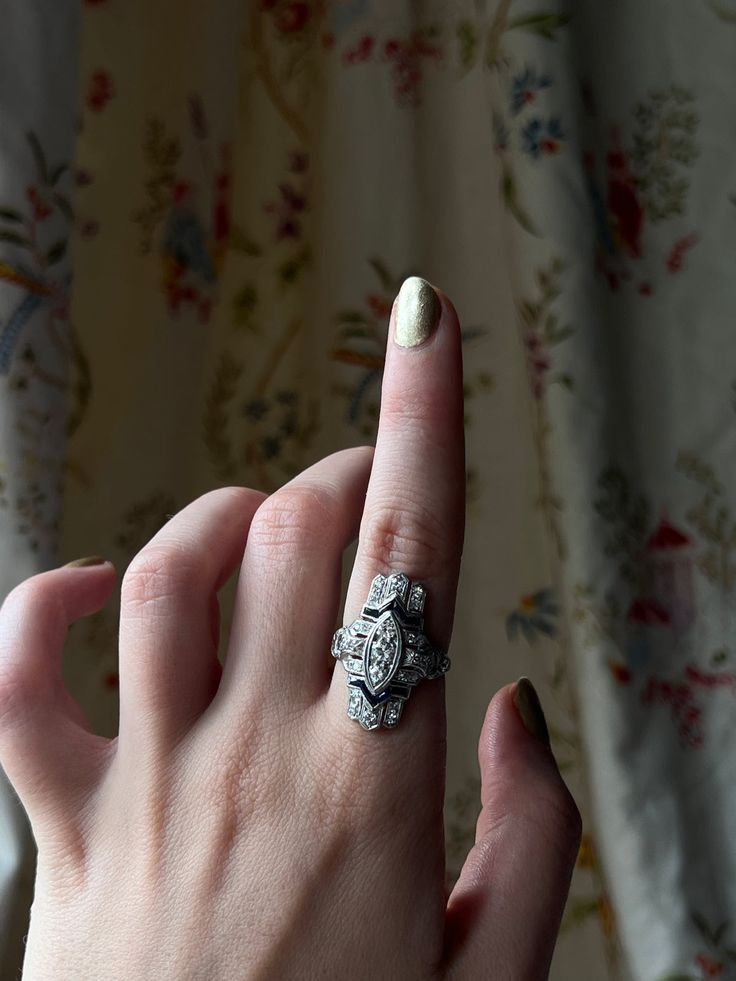 a woman's hand with a ring on it and a flowered curtain behind her