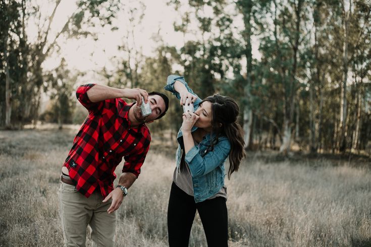 a man and woman standing in a field talking on their cell phones with trees in the background