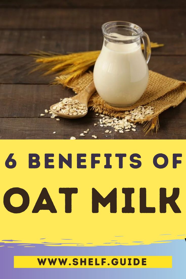 a glass jar filled with oat milk on top of a wooden table next to wheat