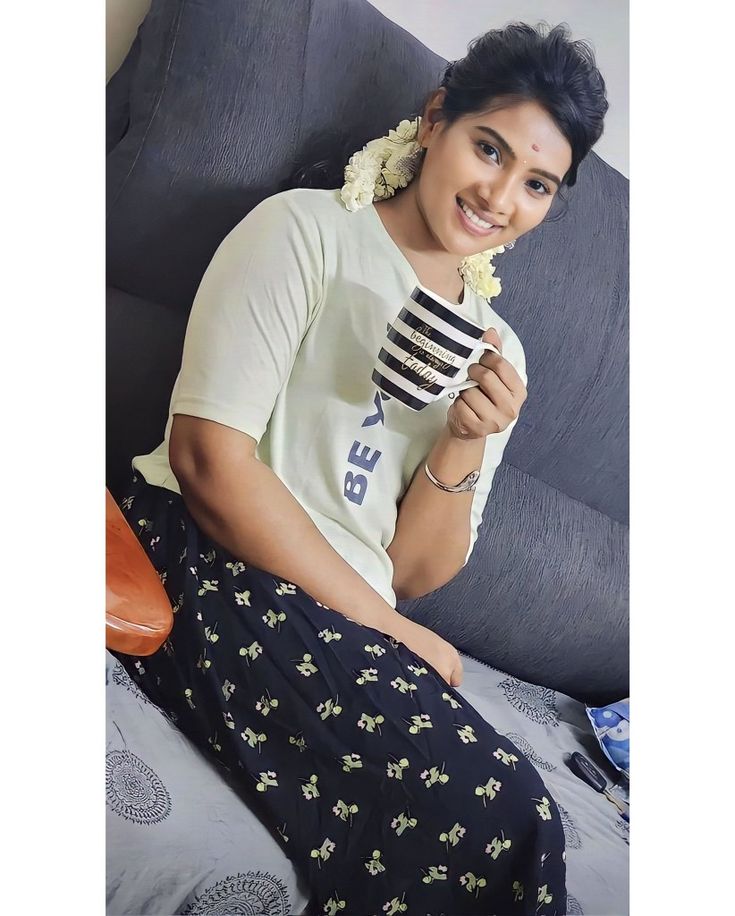 a woman sitting on a bed holding a coffee cup and looking at the camera with a smile