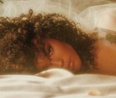 a close up of a person laying on a bed with a white sheet and hair