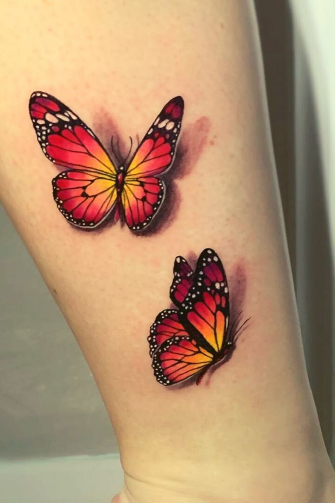 two red and yellow butterflies on the side of a woman's leg, both with black dots