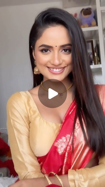 a woman with long hair wearing a red and gold sari, smiling at the camera